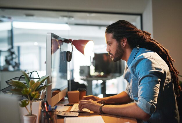 Solo quedan algunos toques finales Captura recortada de un joven diseñador trabajando hasta tarde en una computadora en una oficina