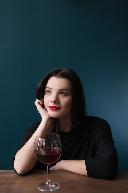 Solo soñando joven mujer en bar. Perspectivas futuras en la vida, estado de ánimo melancólico con vino tinto sobre fondo azul con espacio libre, concepto de sueño