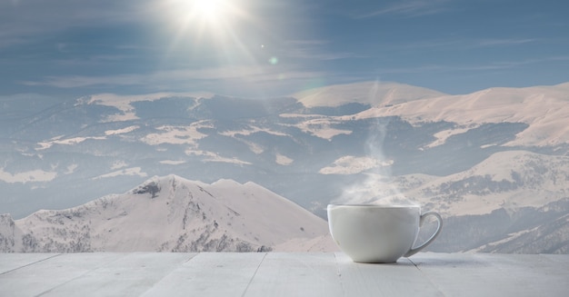 Solo taza de té o café y paisaje de montañas en el fondo. Taza de bebida caliente con aspecto nevado y cielo nublado frente a él. Cálido en días de invierno, vacaciones, viajes, Año Nuevo y Navidad.