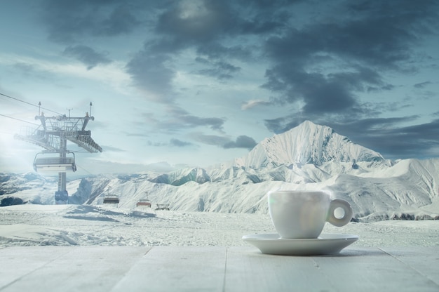 Solo taza de té o café y paisaje de montañas en el fondo. Taza de bebida caliente con aspecto nevado y cielo nublado frente a él. Cálido en días de invierno, vacaciones, viajes, Año Nuevo y Navidad.