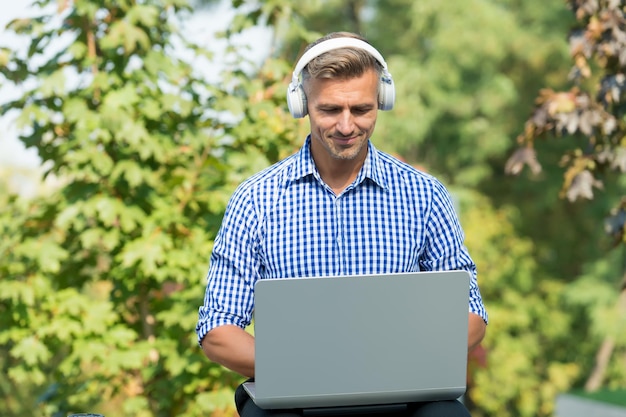 Solo yo y mi computadora. Hombre guapo usa computadora al aire libre. Computadora para negocios y juegos. Computadora personal portátil. Auriculares portátiles. Nueva tecnología. Vida moderna. Estilo de vida móvil.