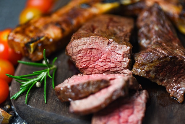 Solomillo de ternera asado con hierbas y especias servido con vegetales sobre tabla de madera - rebanada de carne de res a la parrilla sobre fondo negro