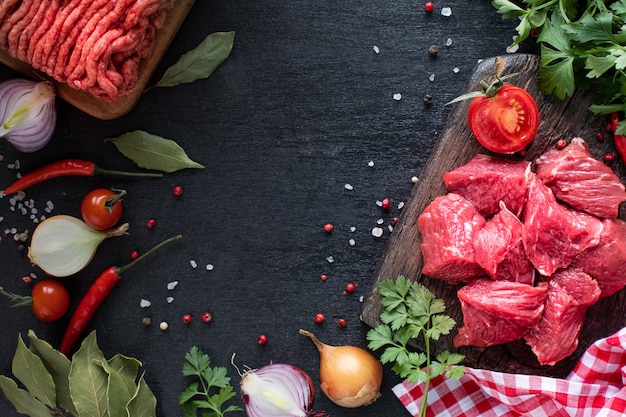 Solomillo de ternera y carne picada en una tabla de cortar de madera con tomates cherry, pimiento picante y hierbas.