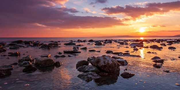 Soltando o pôr do sol de longa exposição sobre o mar com uma praia rochosa