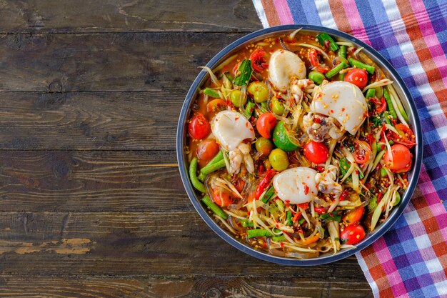 Som Tam Seafood-Tintenfisch (würziger Papaya-Salat) mit gesalzener Krabbe, auf Holztisch