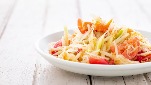 Som Tum Thai, Som Tam Thai, comida tailandesa, ensalada de papaya picante con cobertura de tomate, lima y chile con camarones secos sobre fondo blanco de textura de madera vieja, fotografía de comida ligera y aireada