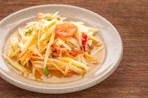 Som Tum Thai, Som Tam Thai, comida tailandesa, ensalada de papaya picante con cobertura de tomate, lima y chile con camarones secos sobre fondo de textura de madera natural, vista superior