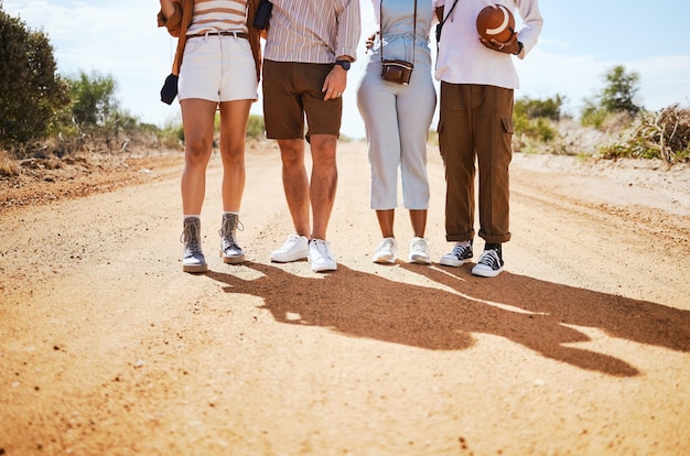 Sombra de sapatos e amigos em uma estrada de areia no deserto para férias de verão ou férias enquanto caminham juntos na natureza Pernas de viagem e aventura com um grupo de homem e mulher em pé em uma trilha