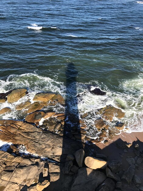 Sombra de um homem de pé em uma rocha ao lado do mar