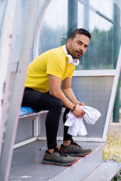 À sombra do caramanchão no estádio de esportes da cidade, o homem de esportes relaxa na cadeira, fones de ouvido e toalha