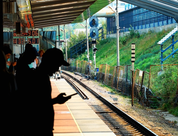 Sombra del hombre que consume contenido móvil en el fondo de la estación de tren