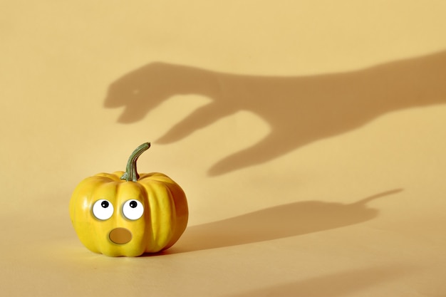 La sombra de la mano alcanza la calabaza con los ojos. Feliz Halloween. Concepto mínimo de Halloween.