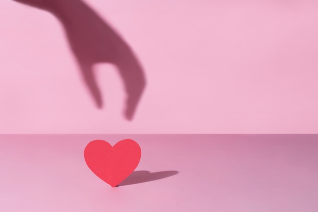 La sombra de una mano femenina tomando un corazón rojo.