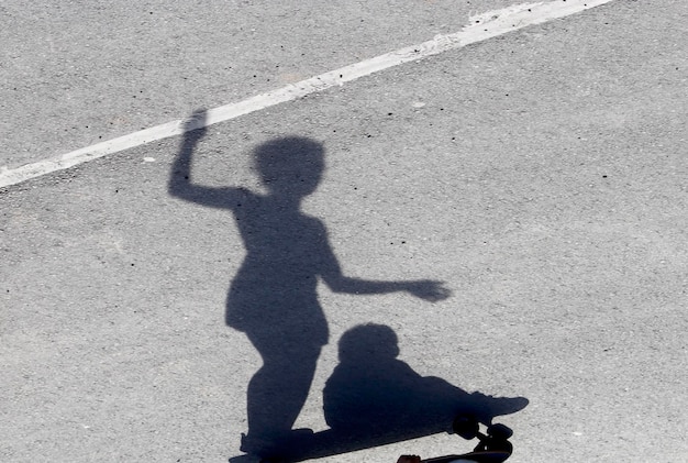 Foto sombra de una niña con un niño en patinaje en la calle durante un día soleado