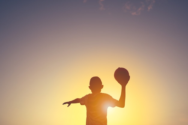 Sombra de los niños en la puesta del sol sosteniendo la pelota para jugar en el fondo del cielo