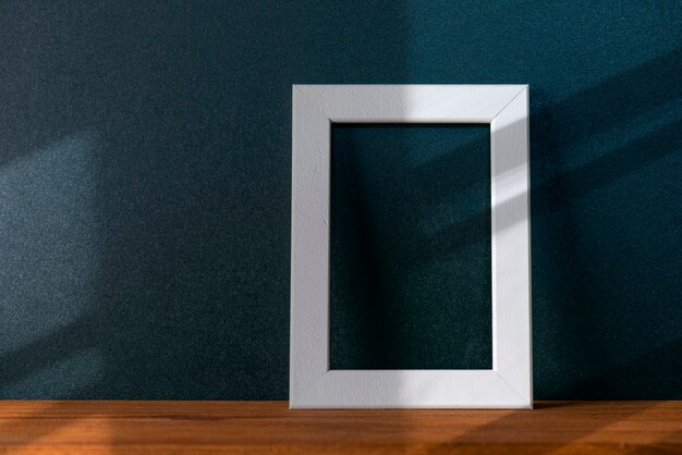 Sombras abstratas de linhas na parede preta na sala com interior mínimo. Composição com moldura branca em branco na mesa de madeira, maquete de decoração, espaço para texto