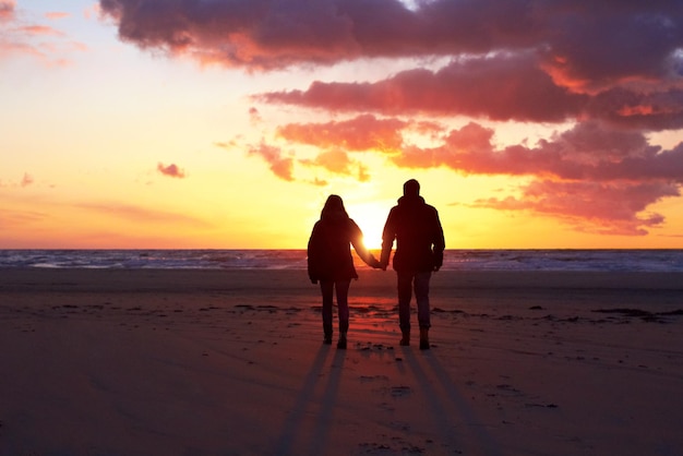 Sombras no pôr do sol Silhueta de um casal indo passear na praia ao pôr do sol