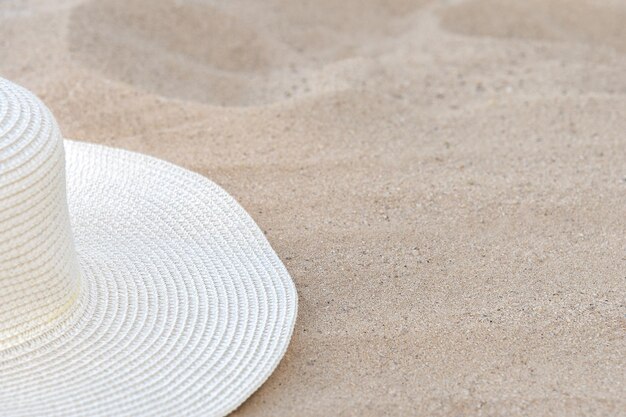 Un sombrero blanco de paja femenino se encuentra en una playa de arena amarilla bajo la luz del sol