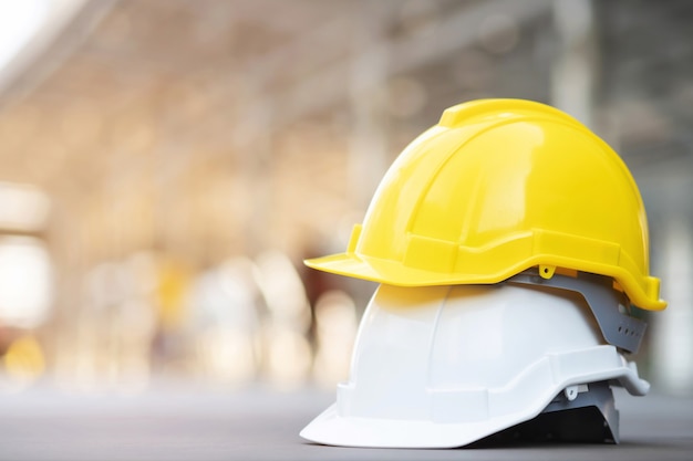 Sombrero de casco de uso de seguridad duro amarillo y blanco en el proyecto en el edificio del sitio de construcción en piso de concreto con luz solar. casco para obrero como ingeniero o trabajador. concepto de seguridad primero.