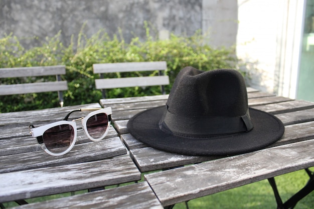 Foto sombrero fedora y gafas de sol en mesa exterior de madera.