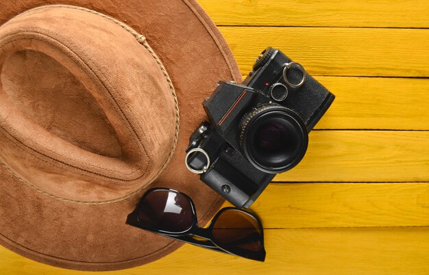 Sombrero de fieltro, cámara de cine, diseño de gafas de sol en una mesa de madera de color. Pasión por viajar, concepto de pasión por los viajes. Endecha plana.