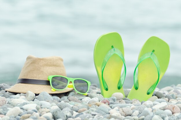 Sombrero, gafas y chanclas en la playa de guijarros.