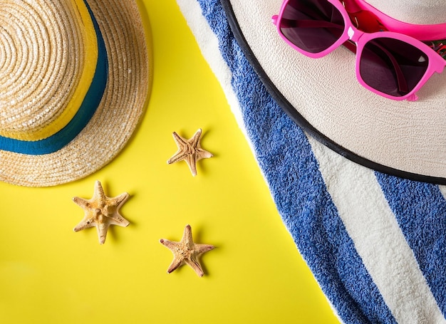 Un sombrero, gafas de sol y estrellas de mar están sobre una toalla amarilla y azul.