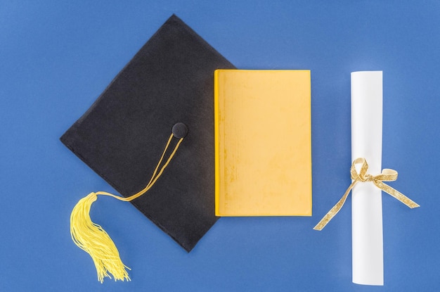 Foto sombrero de graduación con diploma y libro aislado en azul