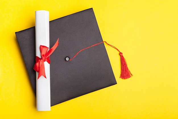 Foto sombrero de graduación y diploma sobre fondo amarillo