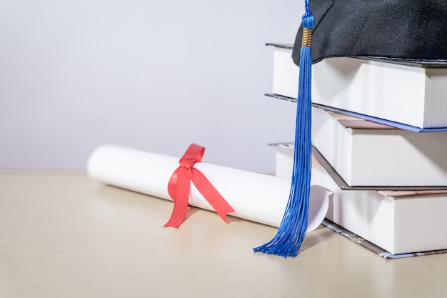 Foto sombrero de graduación con libros y diploma sobre la mesa contra backgrou blanco