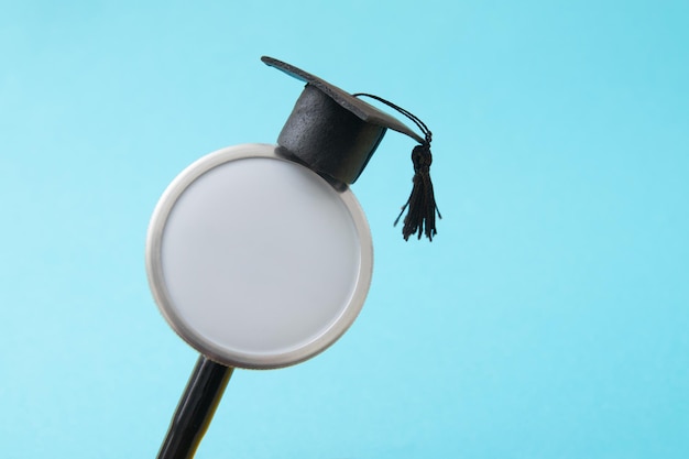 Sombrero de graduación en maqueta de estetoscopio médico, fondo azul. Facultad de medicina, educación sanitaria o concepto de título universitario de doctor