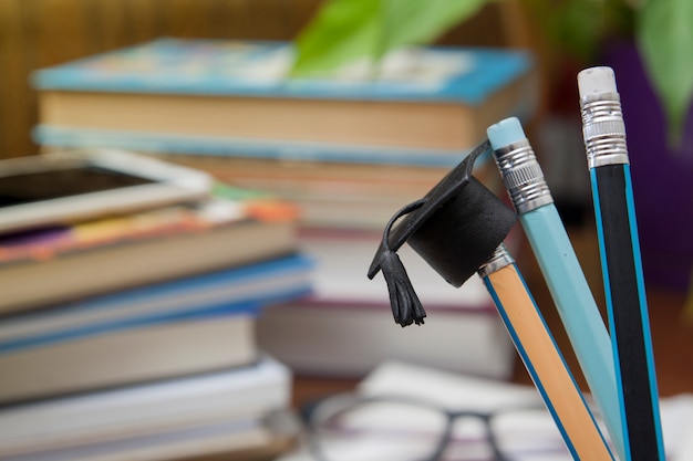 Sombrero graduado en un lápiz, libros y gafas. Concepto de educación