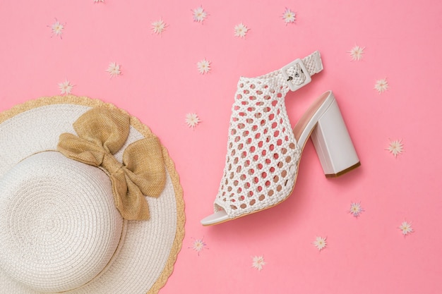 Sombrero de moda con lazo y zapato de cuero trenzado blanco sobre fondo rosa con flores