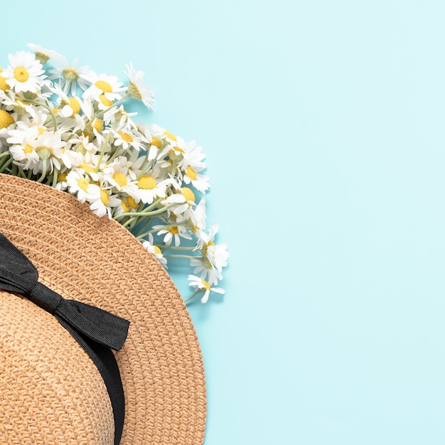 Sombrero de mujer y flores de manzanilla sobre fondo azul.