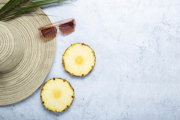 Sombrero de mujer, gafas de sol, rodajas de piña, hoja de palma sobre un fondo de hormigón. Vista superior, endecha plana.