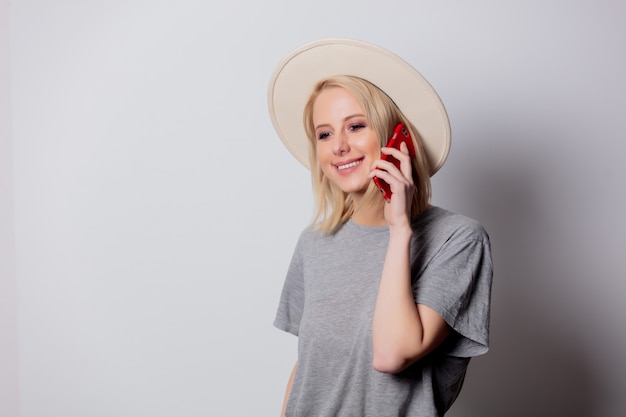 Sombrero de mujer rubia con teléfono móvil en la pared blanca