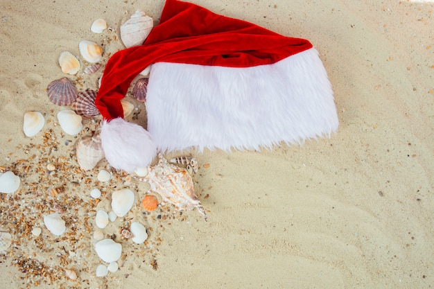 Sombrero de Navidad en la playa. Sombrero de Santa en la arena cerca de conchas.