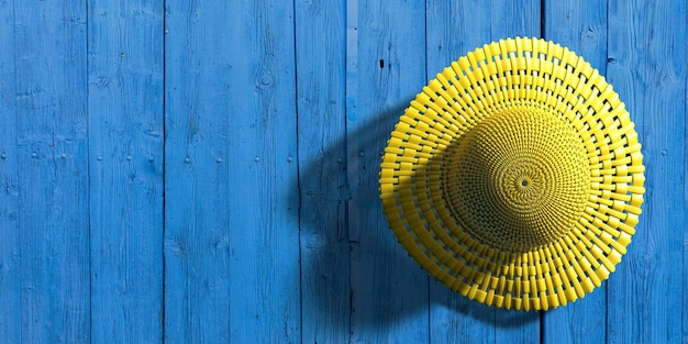 Sombrero de paja amarillo sobre fondo de tablero de madera azul protección solar de verano ilustración 3d
