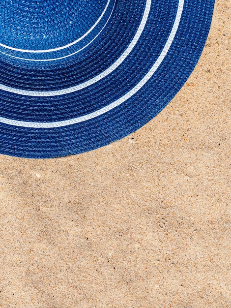 sombrero de paja azul con rayas blancas se encuentra en la arena de la playa Concepto de vacaciones junto al mar