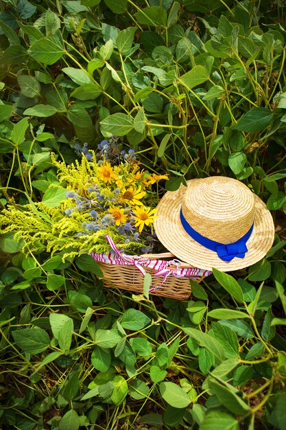 Sombrero de paja y canasta con flores en la hierba