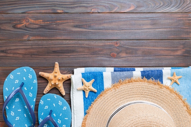 Sombrero de paja, chanclas azules, toalla y estrella de mar sobre un fondo de madera oscura. concepto de vacaciones de verano de vista superior con espacio de copia.