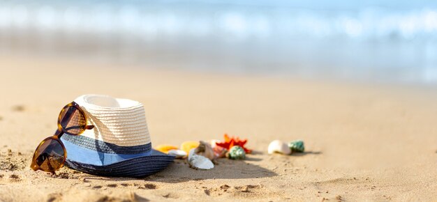 Sombrero de paja, conchas y gafas de sol en una playa tropical, espacio de copia