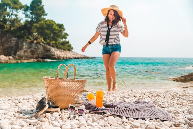 Sombrero de paja de cosas de playa y bolsa con aletas y crema de protección solar en la mujer de la orilla del mar en el fondo