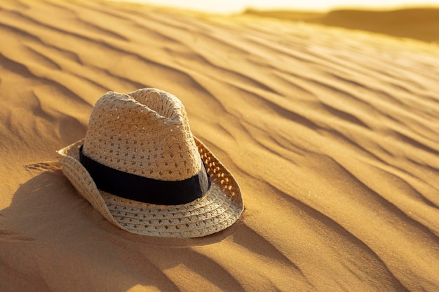 Sombrero de paja se encuentra en las dunas de arena en la arena del desierto naranja al atardecer