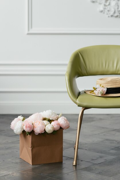 Sombrero de paja se encuentra en un sillón verde junto a un ramo de flores contra un fondo de pared