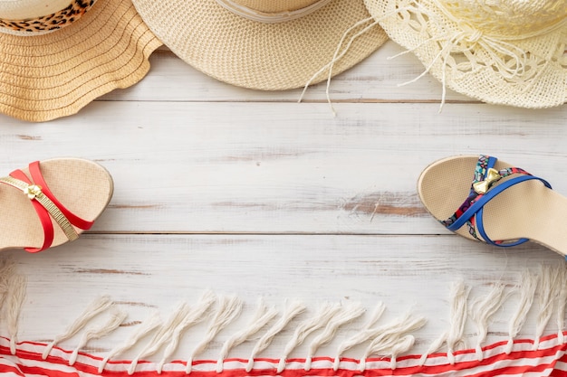Sombrero de paja de fondo de verano, sandalias, pareo con flecos sobre un fondo de madera clara