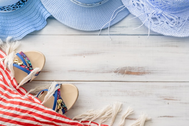 Sombrero de paja de fondo de verano, sandalias, pareo con flecos sobre un fondo de madera clara