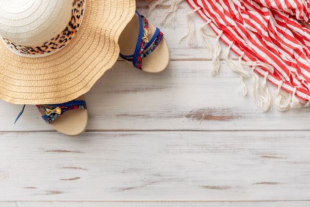 Sombrero de paja de fondo de verano, sandalias, pareo con flecos sobre un fondo de madera clara