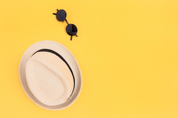 Sombrero de paja y gafas de sol sobre un fondo amarillo.