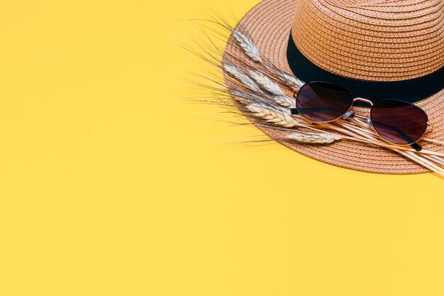 Sombrero de paja marrón con gafas de sol y espigas secas de trigo en amarillo